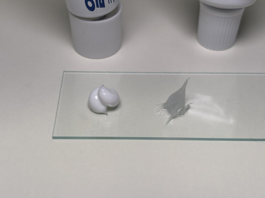 유리 위에 엘리델 크림(불투명 흰색)과 프로토픽 연고(반투명 젤리상)를 나란히 짜서 텍스처와 점도 차이를 클로즈업으로 비교한 사진 — 환자의 제형 선택 시 참고